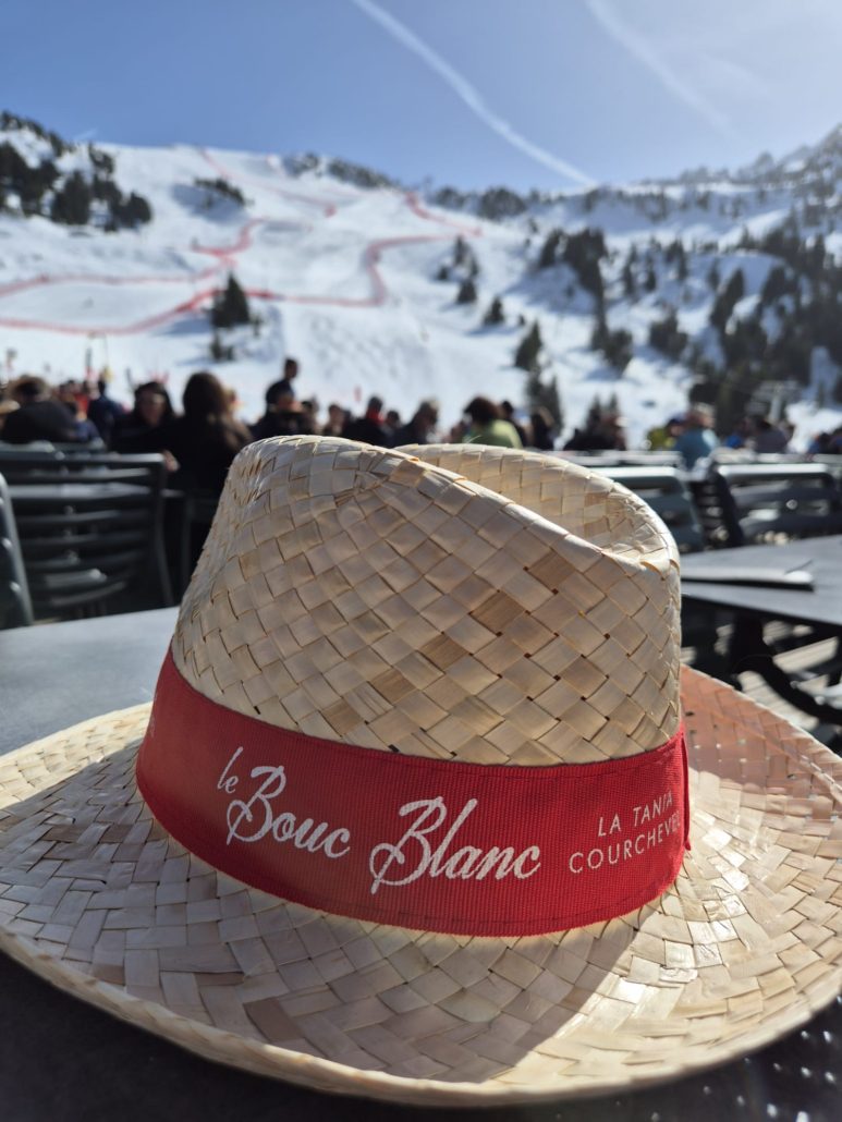 Straw sun hat on a restaurant terrace table with snowy ski slopes in the background