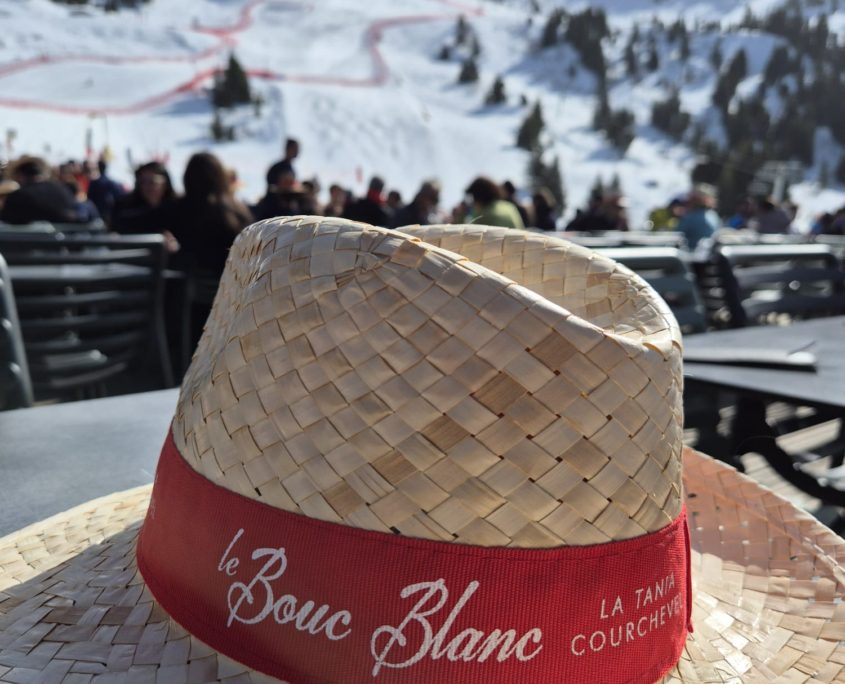 Bouc Blanc hat Straw sun hat on a restaurant terrace table with snowy ski slopes in the background