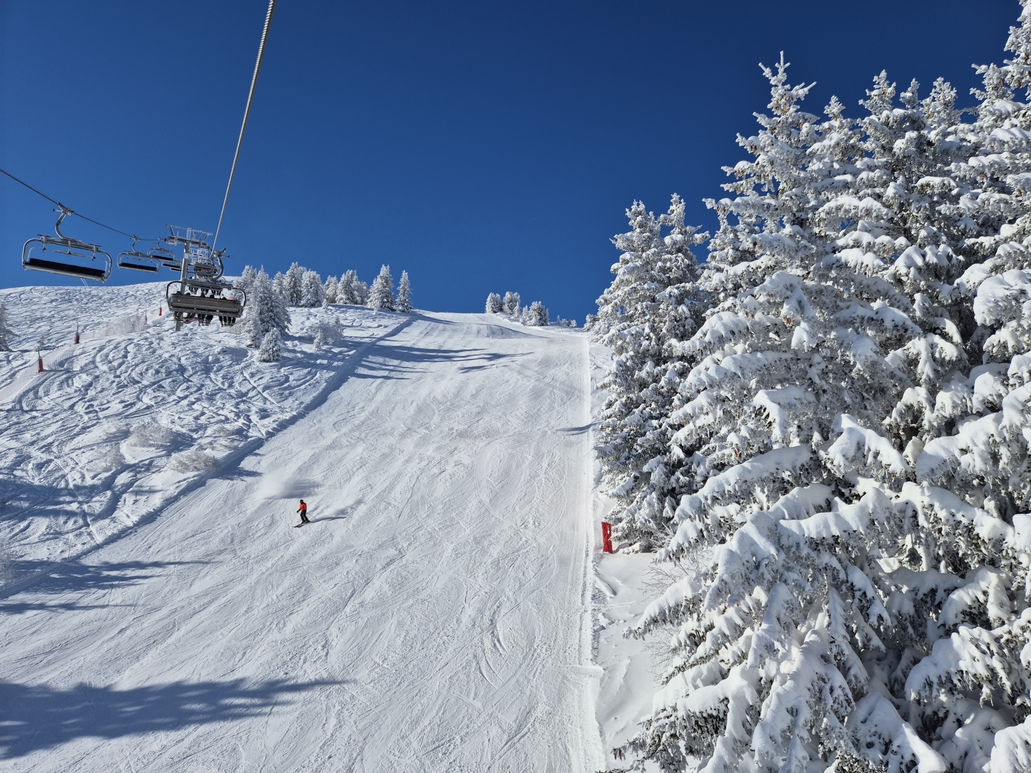 A ski run in the French resort of Courchevel, surrounded by snow-covered pines against a blue sky.