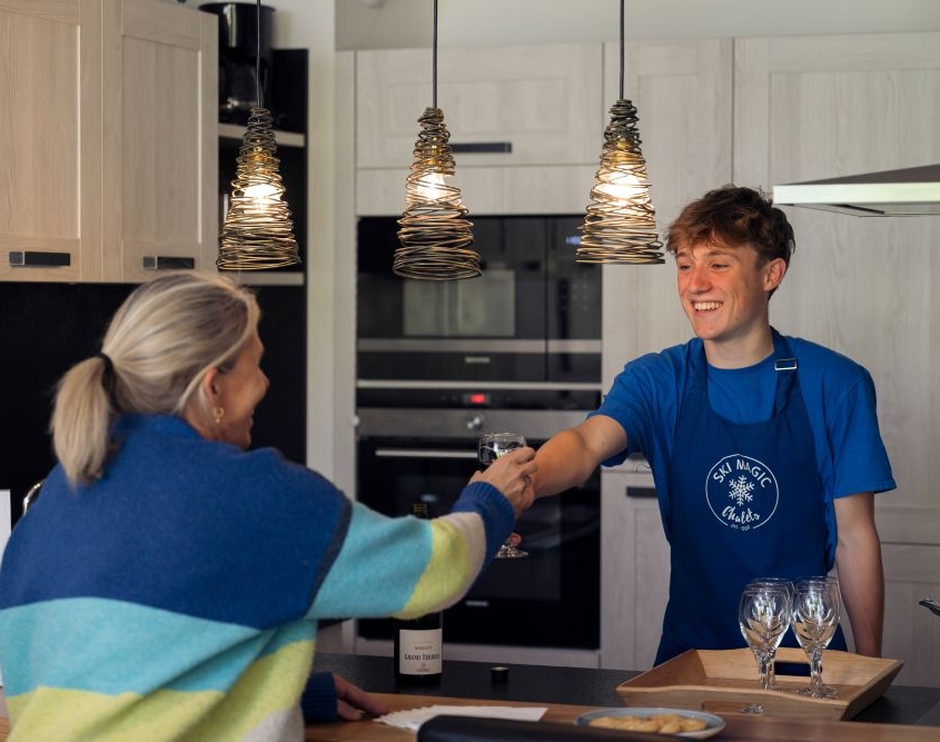 What's new in the Three Valleys this winter? 2 Ski Magic chalet host hands guest a glass of wine in the kitchen of Chalet Caroline, La Tania