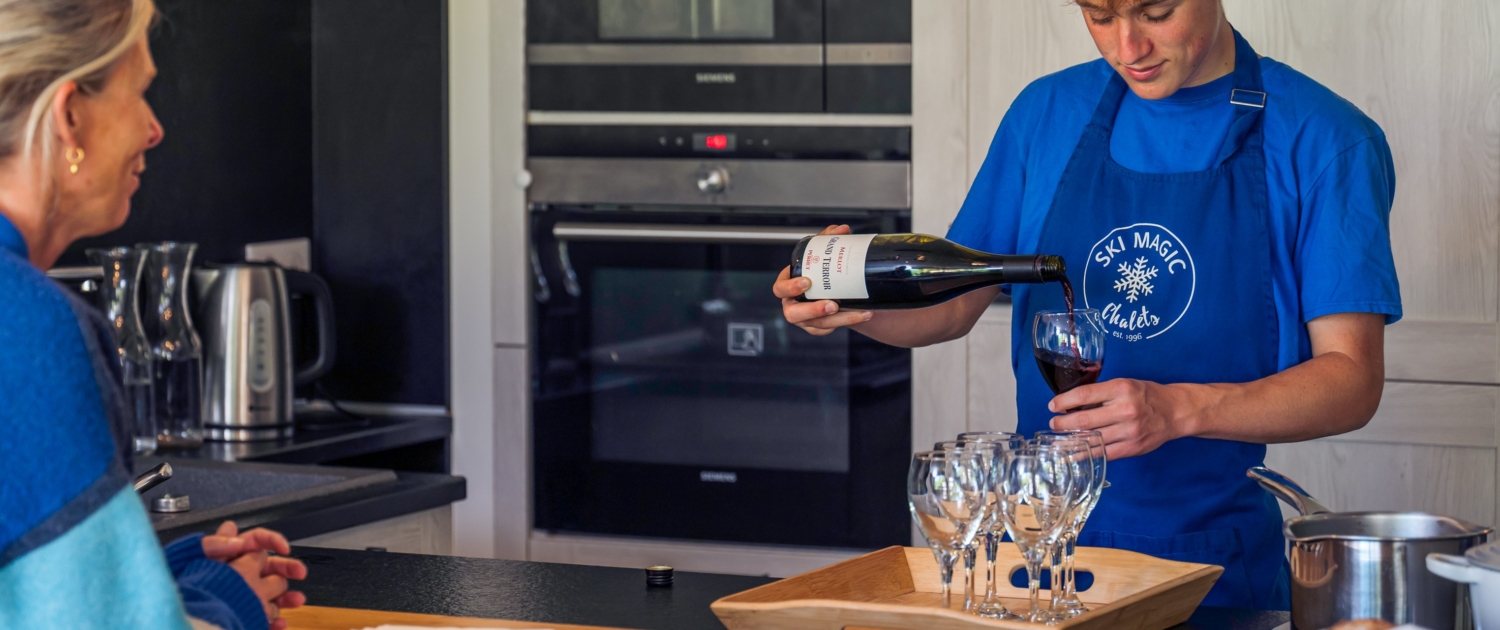 Chalet host pouring wine for a guest in a ski chalet.